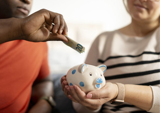 Two people putting money into piggy bank